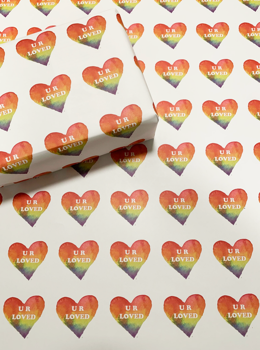 wrapping paper that has rainbow colored hearts with U R loved copy in a repeated pattern