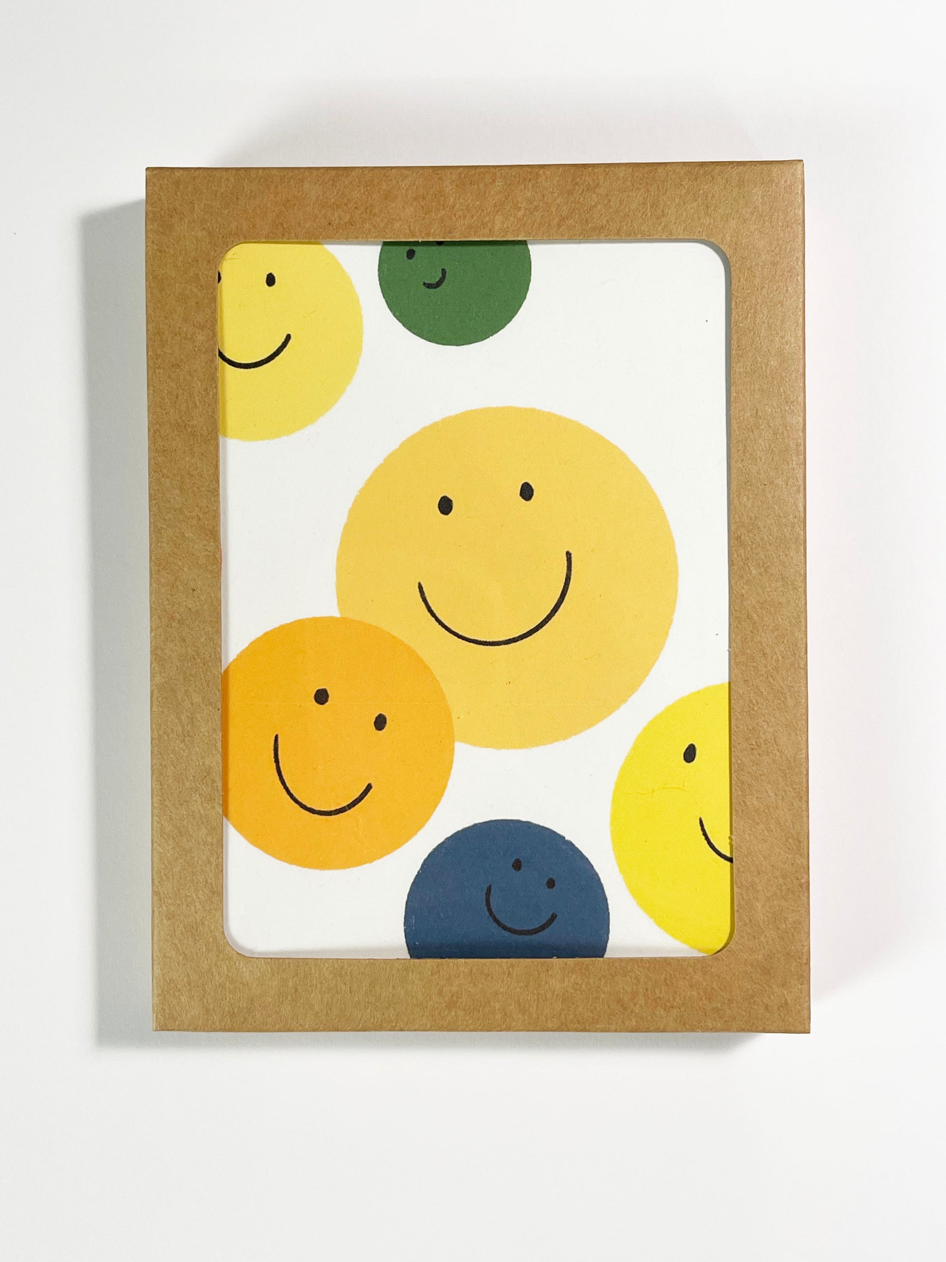 yellow, green, blue and orange smile faces on a greeting card, blank inside, shown in a boxed card packaging