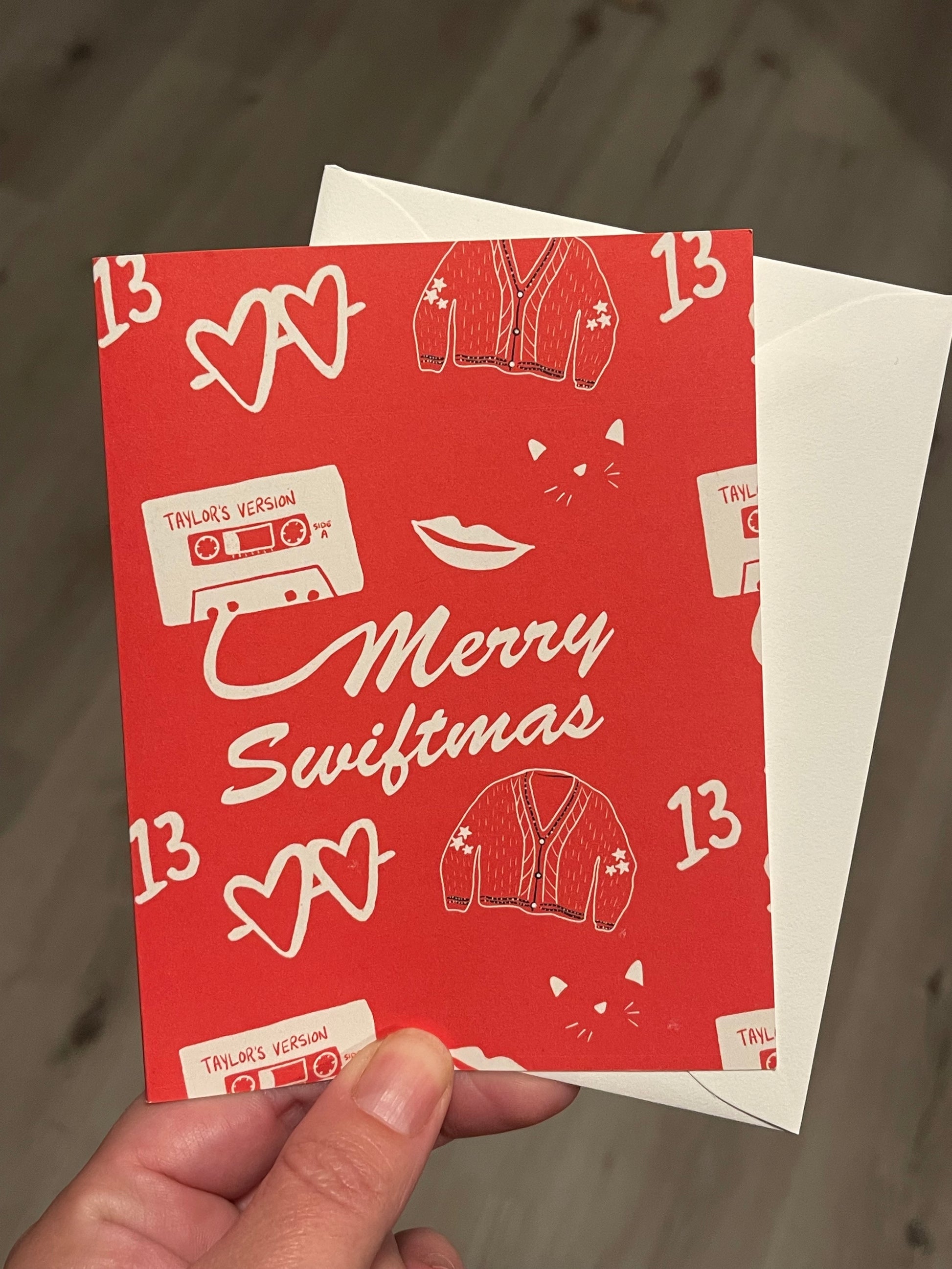 Greeting card that reads merry swiftmas on the front with taylor swift inspired icons on a red background