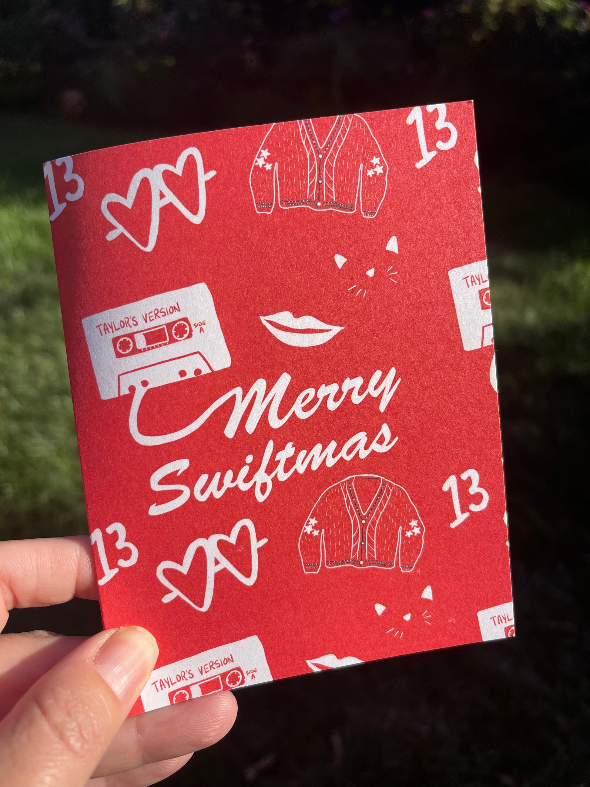 Greeting card that reads merry swiftmas on the front with taylor swift inspired icons on a red background