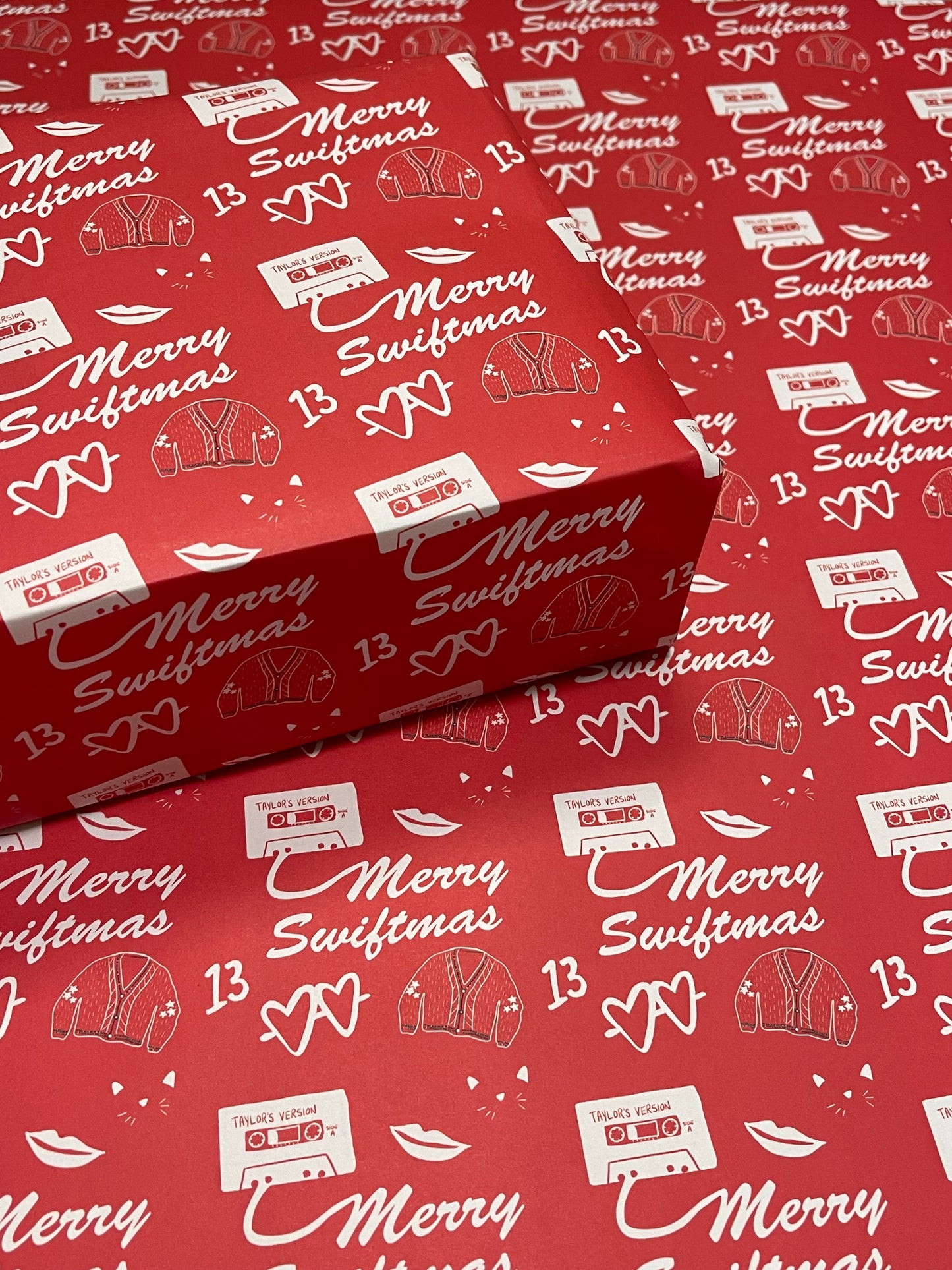 Wrapping paper that reads merry swiftmas with taylor swift inspired icons in white on a red background.