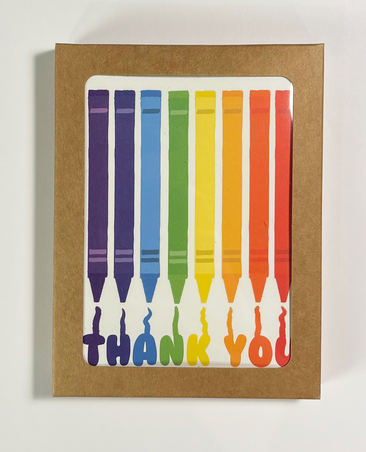 Greeting card with multiple crayons in rainbow shade that reads thank you. blank inside, shown in a boxed card set